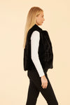 Side view of model wearing the Dolce Cabo Faux Fur Vest in Black, featuring a cozy fold-over collar and pockets