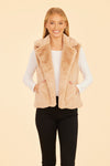 Smiling model in the Dolce Cabo Faux Fur Vest - Champagne. A light beige fur vest with a fold over collar and pockets. 