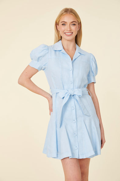 Smiling model in short light blue dress, with collar, buttons down the front, puff sleeves, and belt 