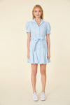 Full view of model in short light blue dress with a collar, buttons down the front, puff sleeves and a belt 