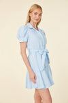 Model in a short blue dress with a collar, buttons down the front, puff sleeves, and a belt