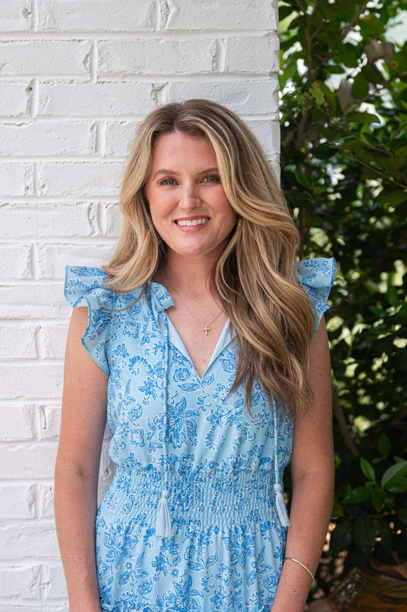 Model wearing a tiered maxi dress in a blue floral print with a ruched waist and flutter sleeves.