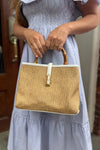 Model outside holding the Chatham Straw Bag - White. A woven bag with white trim and a bamboo handle 