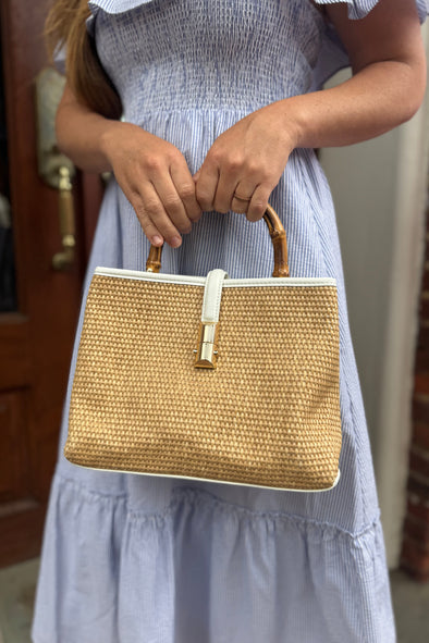 Model outside holding the Chatham Straw Bag - White. A woven bag with white trim and a bamboo handle 
