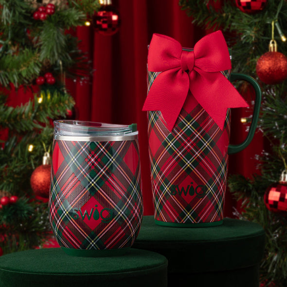 Two plaid tumblers with red bows on a green surface with Christmas tree in the background
