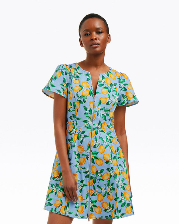 Model in the Draper James Mae Love Circle Dress - Lemon Blossom. A mini short sleeve dress with a zipper front closure and a lemon pattern on a light blue background