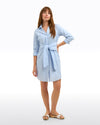 Model standing in the Draper James Isabella Shirt Dress - Oxford Shirting. A light blue striped shirt dress with a tie waist and long sleeves that have been cuffed 