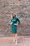Woman in a green dress standing against a brick wall