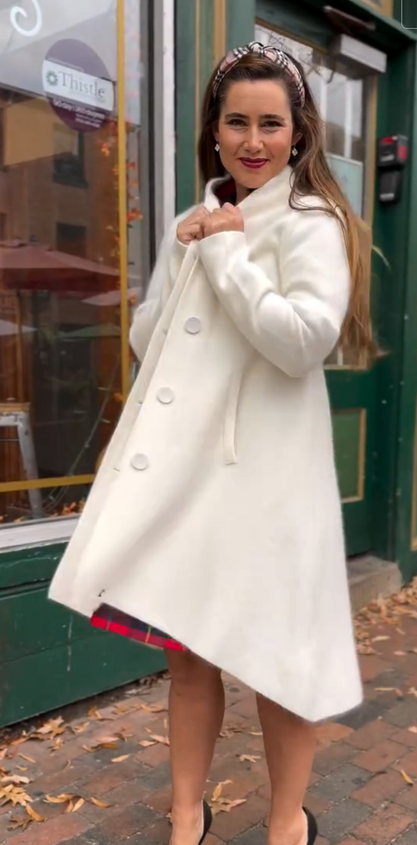 Woman wearing a white coat standing on a street with a building in the background