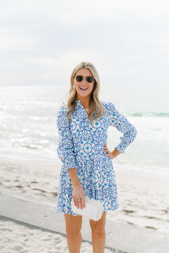 Model in Sail to Sable Long Sleeve Tunic Flare Dress in Medallion on beach with white clutch