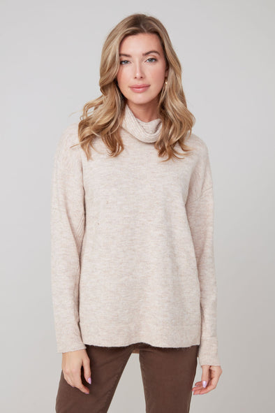 Woman wearing a beige sweater with a cowl neck with a plain background