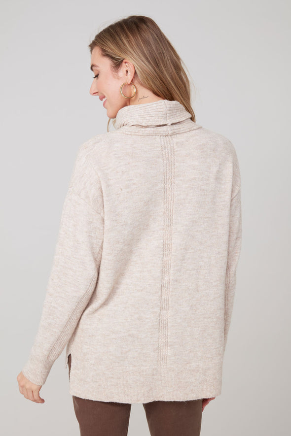 Woman wearing a light beige sweater against a plain background