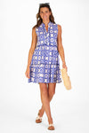 Model in a sleeveless blue tile patterned mini length dress holding a woven bag