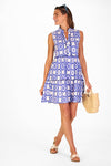 Model in a sleeveless blue tile patterned mini length dress holding a woven bag