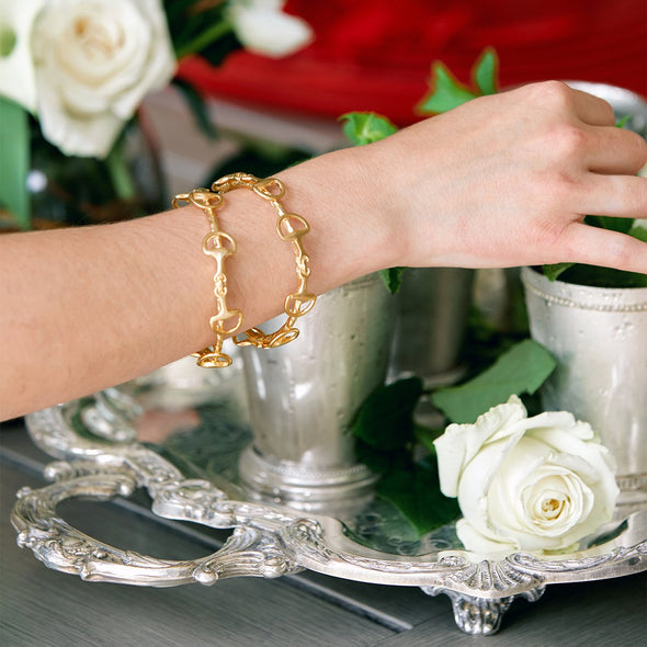 Gold bracelet on a wrist with white roses and silver tray in the background