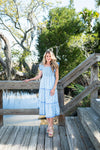 Woman in a blue dress standing on a wooden deck with trees in the background