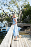 Woman in a blue dress standing on a wooden dock with trees and water in the background