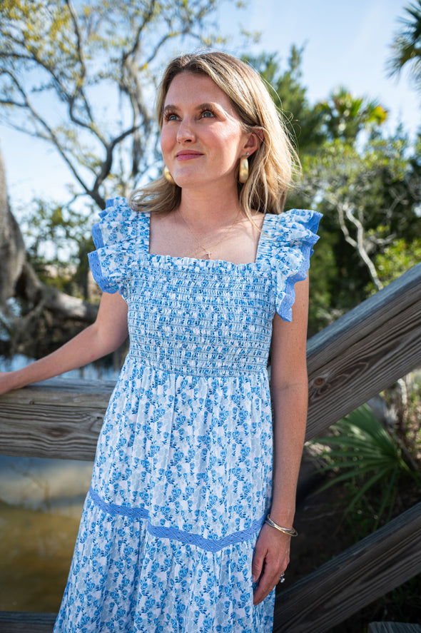 Woman in a blue floral dress standing outdoors with trees in the background