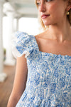 Woman wearing a blue and white patterned dress with ruffled sleeves.
