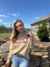 Person wearing a beige sweatshirt with text, standing outdoors with a clear blue sky.