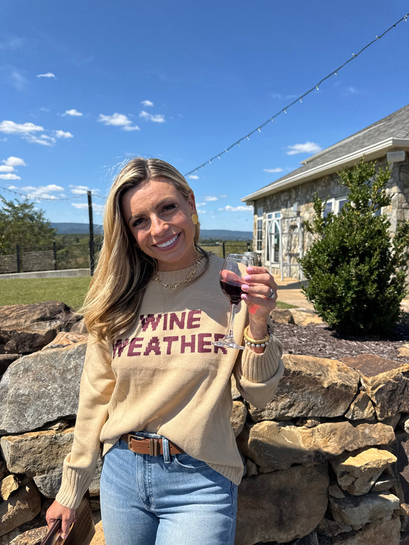 Person wearing a beige sweatshirt with text, standing outdoors with a clear blue sky.