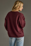 Person wearing a burgundy sweater and light blue jeans against a gray background
