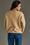 Woman wearing a beige sweater and blue jeans against a gray background