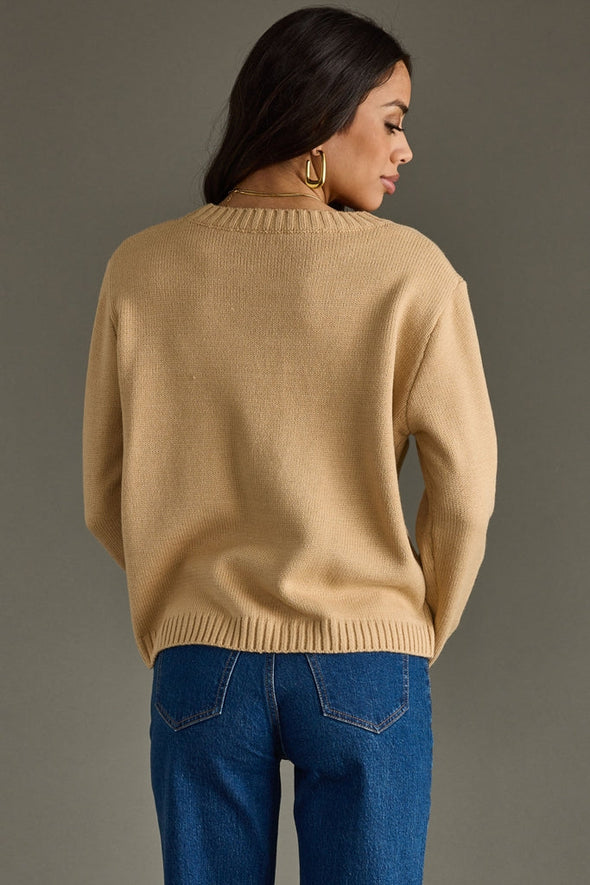 Woman wearing a beige sweater and blue jeans against a gray background