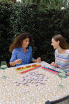 Models playing a board game in the garden in the Duffield Lane Oaklee Dress - Blue Bouquet