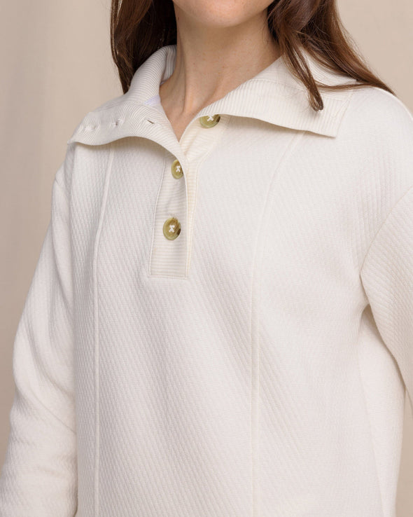 Close-up of a person wearing a white textured sweater with gold buttons on a beige background