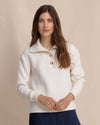 Woman wearing a white jacket with gold buttons against a beige background