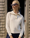Woman wearing a cream-colored sweater with a collar, standing against a wooden wall.
