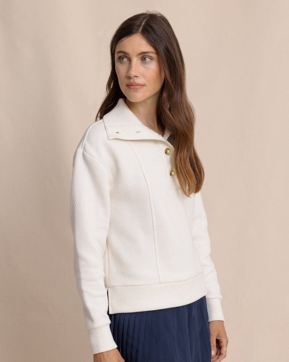 Woman wearing a white jacket with gold buttons against a beige background