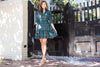 Model in front of a gate in the Gretchen Scott Teardrop Dress in Plaidly Cooper in Green Plaid