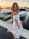 Side view of model on a dock wearing Gretchen Scott Big Love Maxi Dress in White/Gold