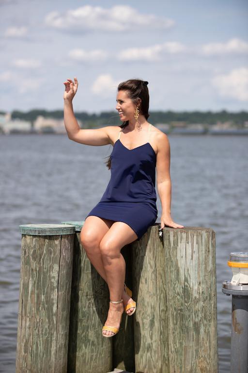 Model sitting on a dock wearing Two models on a dock, right model wearing Jude Connally Bailey Dress in Navy