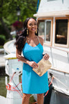 Model wearing Jude Connally Bailey Dress in Santorini Blue wtih gold purse