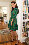 Model leaning against a bookshelf in Gretchen Scotts Teardrop Dress in Plaidly Cooper in Green Plaid